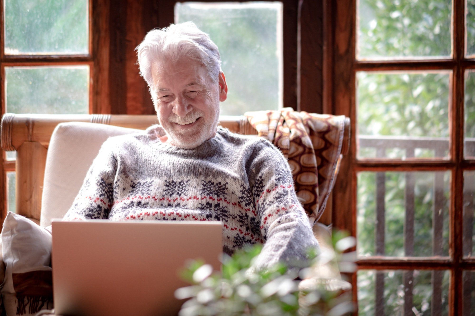 Smiling senior man in winter sweater sitting in living room using laptop computer. Medicare special enrollment period