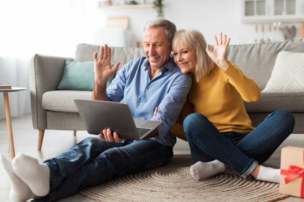 Senior Couple Video Calling Waving Hello To Laptop At Home ready for 2022 Annual Enrollment Period