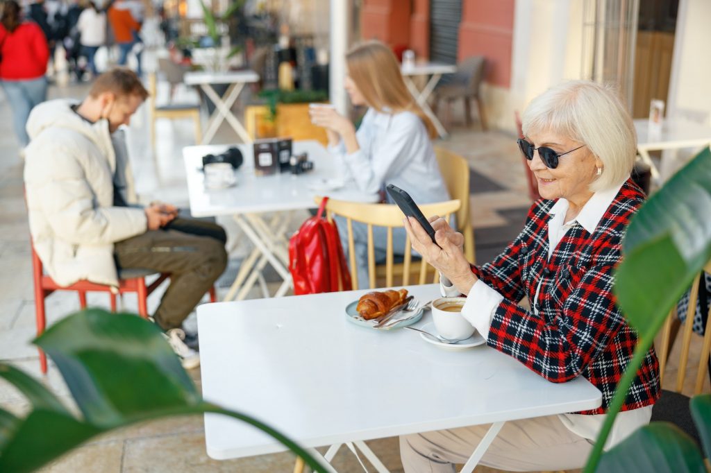 Senior woman using cellphone while having lunch in cafe checking new 2023 Medicare Premiums