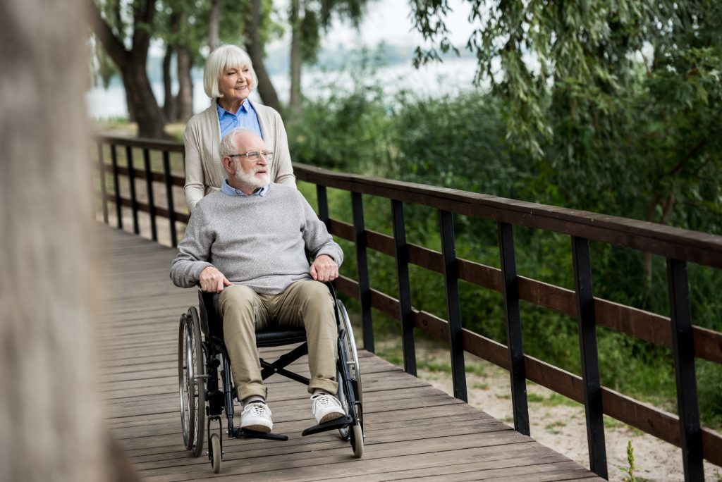 smiling senior woman with husband in wheelchair with Medicare and Social Security Disability