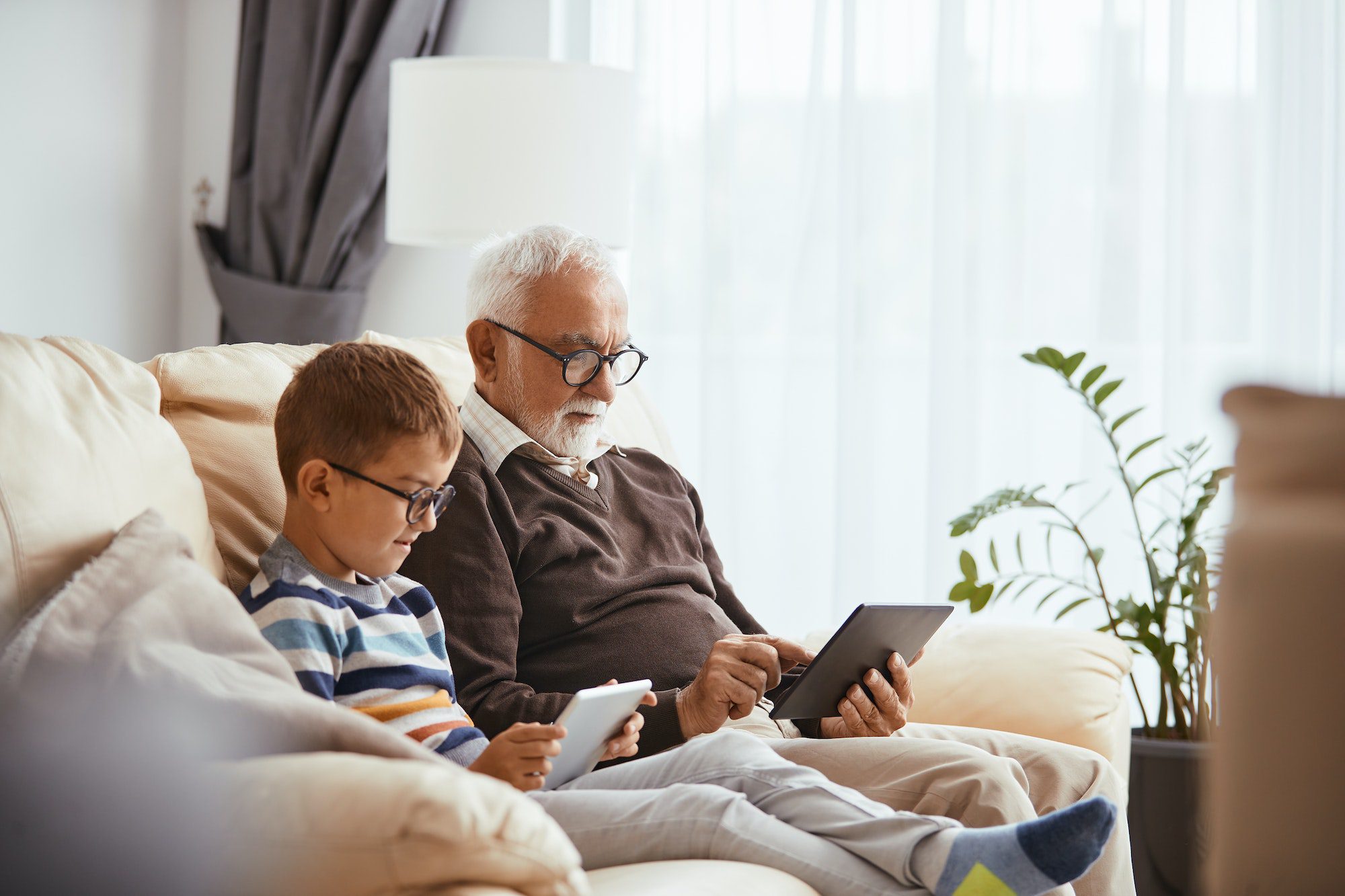 Senior man and his grandson using touchpads while relaxing at home with Medicare and Medicaid