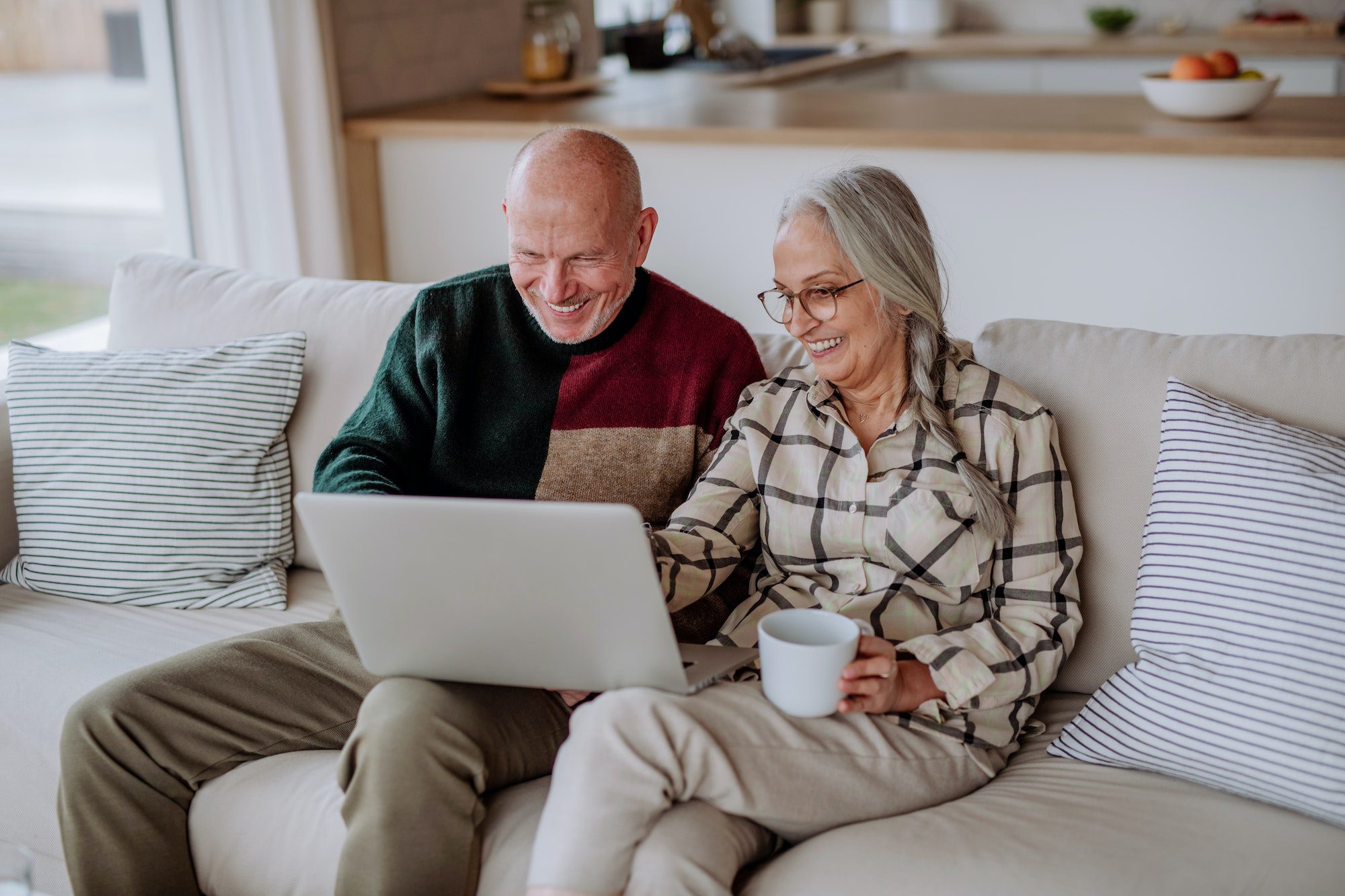 Senior couple sitting on sofa and shopping online with laptop enrolling in Medicare