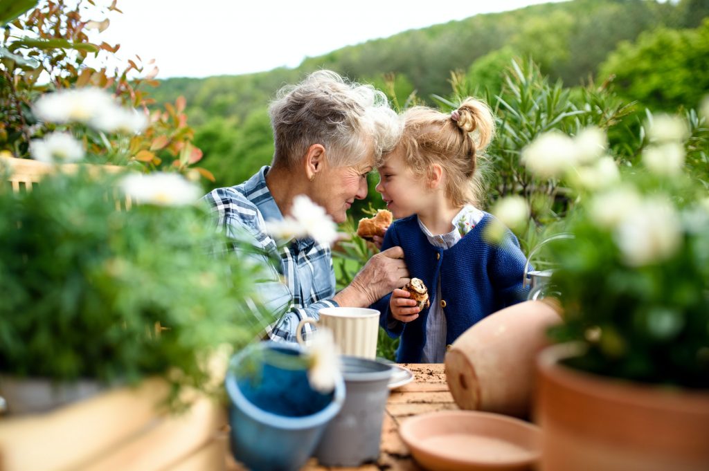 Senior grandmother with small granddaughter gardening on balcony in summer, eating with Medicare Preventive services