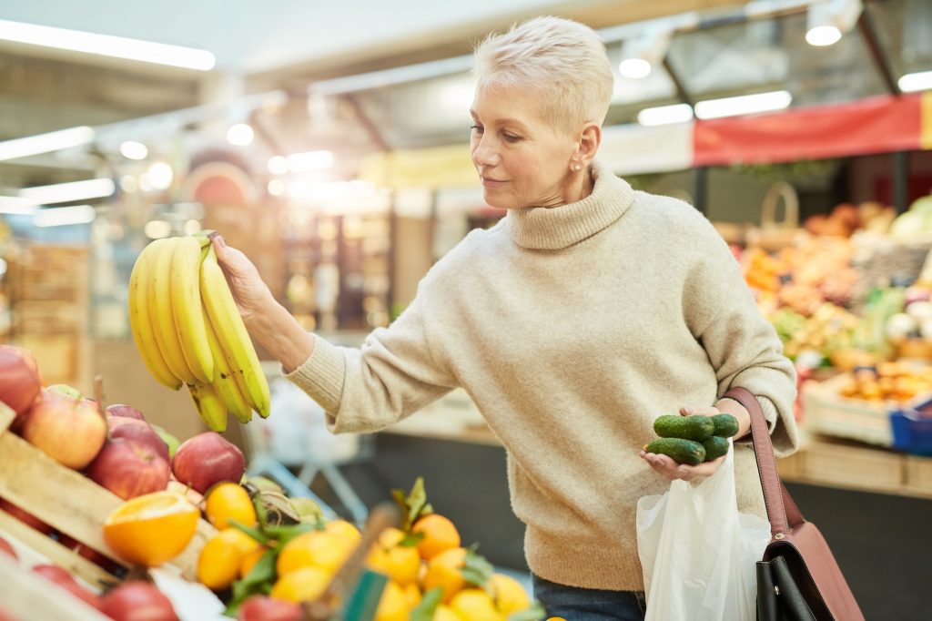 Senior Woman Grocery Shopping at Farmers Market. Saving money on out-of-pocket Medicare Costs
